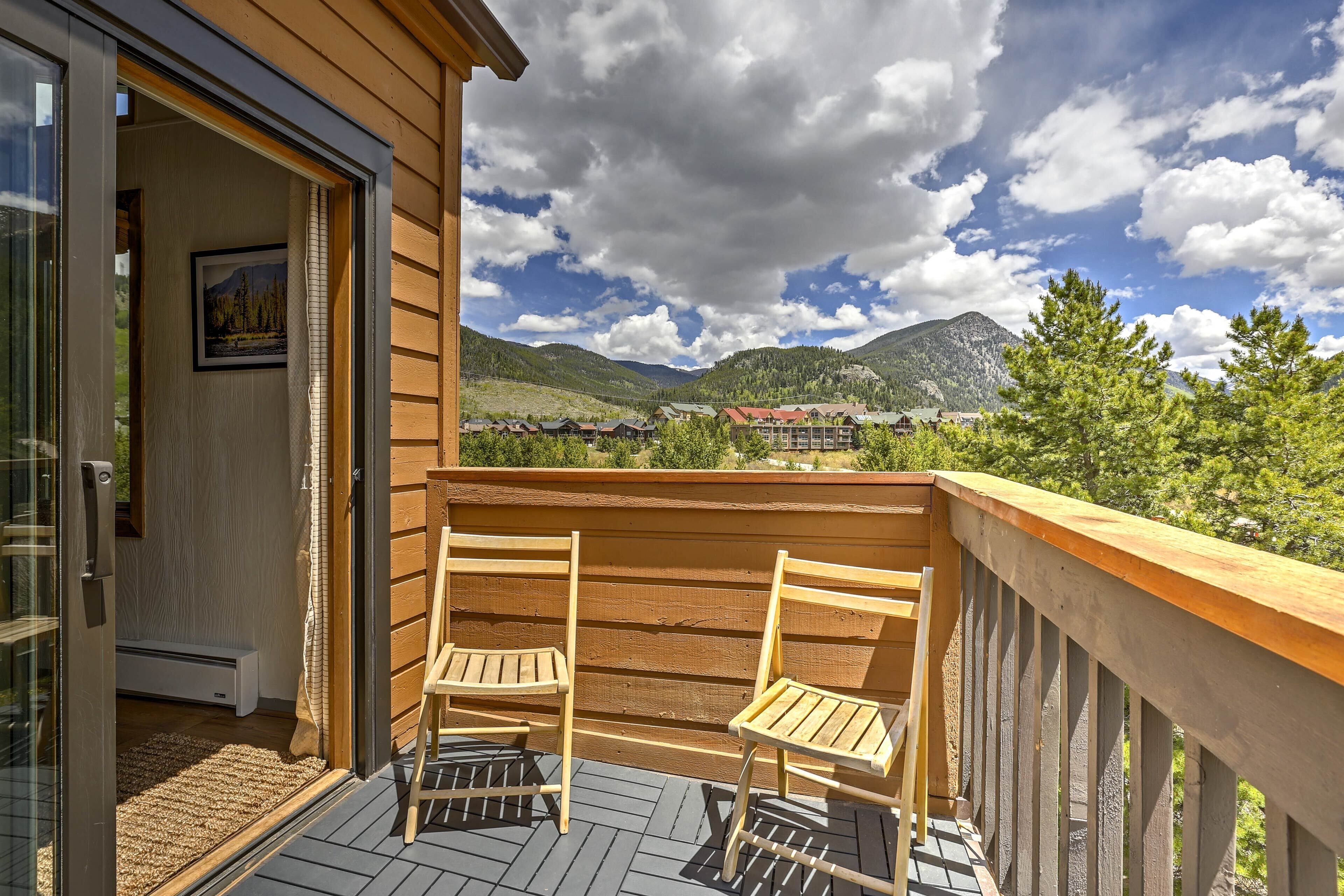 A wooden deck with two chairs and a glass door leading to a room.