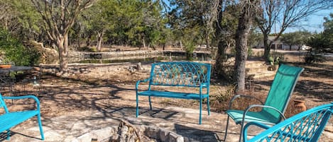 A patio area with a fire pit, blue metal chairs, and a bench.