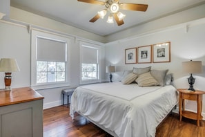 A bedroom with a large bed, two windows, a ceiling fan, and a nightstand with a lamp. - Serene Hill Country Wildlife Sanctuary w/ Porch (Boerne)