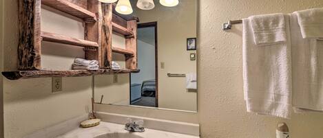 Ein Badezimmer mit Marmorwaschtisch, Holzregalen, einem Spiegel und einer Toilette, an deren Wand ein Handtuch hängt.