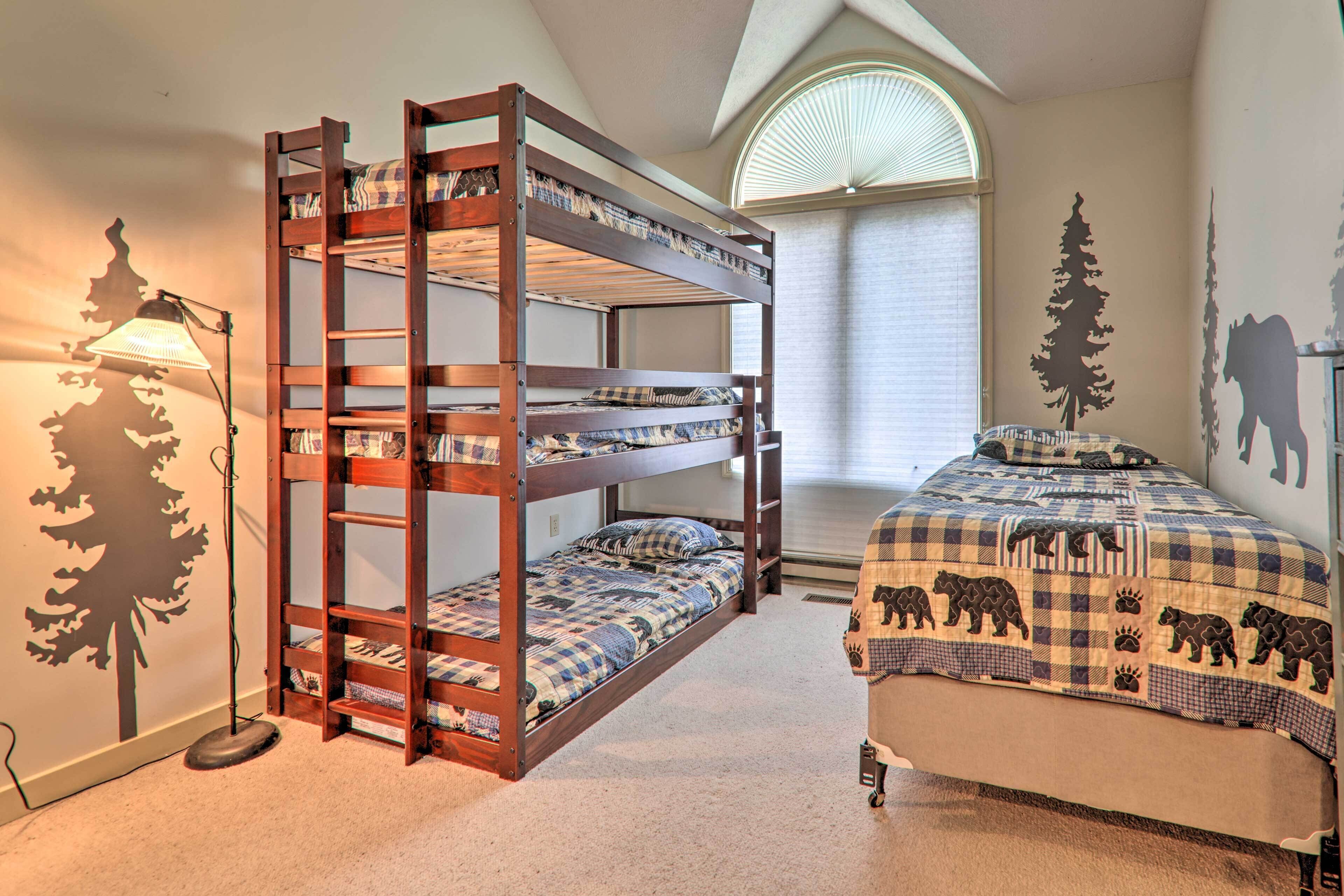 A bunk bed with a checkered bedspread and a single bed with a bear-themed quilt.
