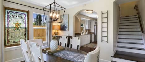A dining area with a round table, white chairs, a chandelier, and a stained glass window.
