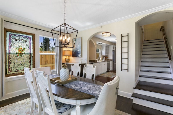 A dining area with a round table, white chairs, a chandelier, and a stained glass window.