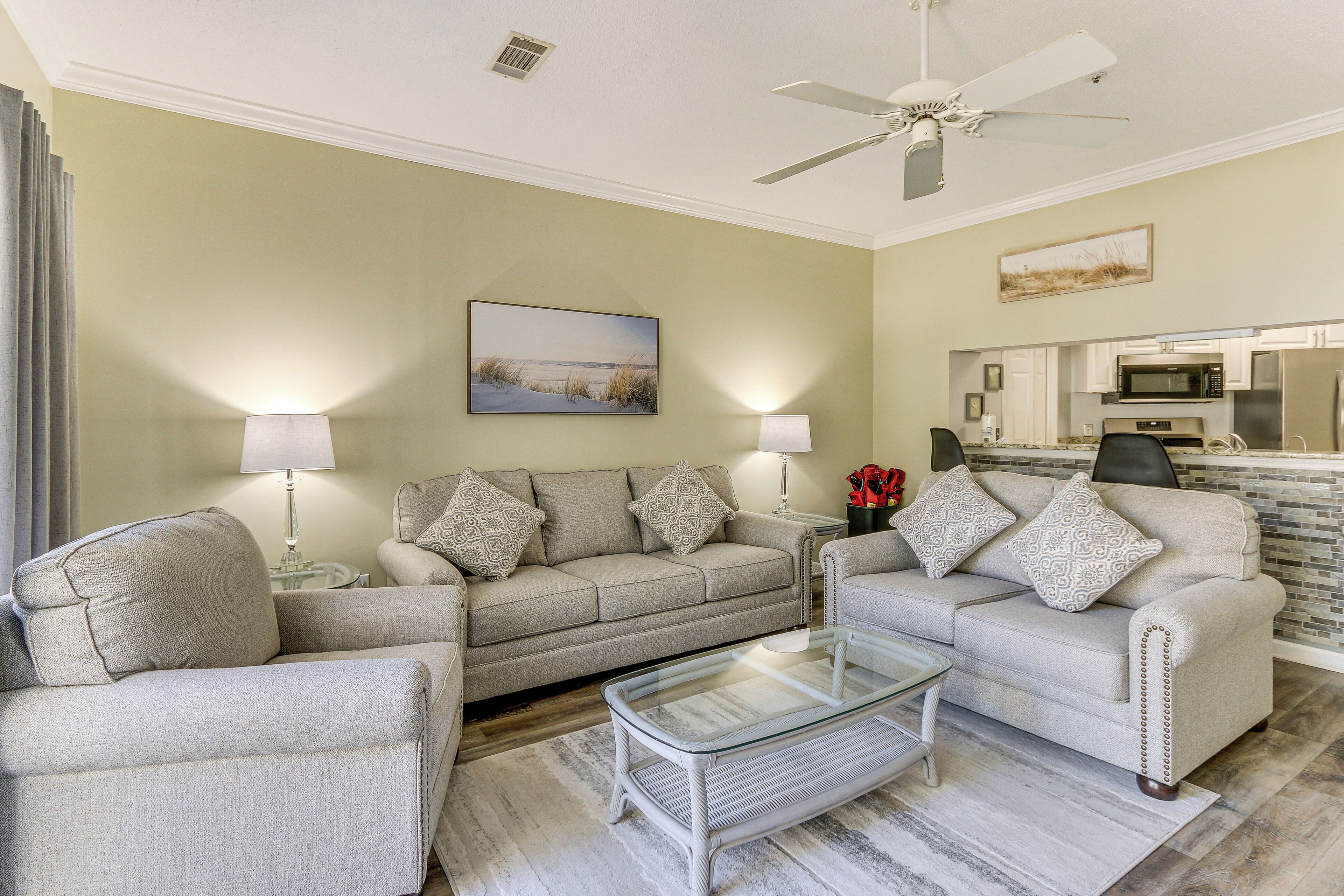 A living room with two sofas, a glass coffee table, and a ceiling fan.