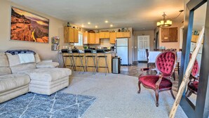 A spacious living room with a large sectional sofa, a red velvet chair, and a kitchen area with wooden cabinets and a bar. - Cottage With Fire Pit + Deck on The Klamath River! (Hornbrook)