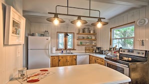 Eine Küche mit Holzschränken, einer weißen Arbeitsplatte, einem Kühlschrank, einem Geschirrspüler, einem Herd und Pendelleuchten.