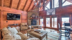 A cozy log cabin interior with a fireplace, leather furniture, and a large window overlooking the outdoors. - Private Eureka Springs Cabin w/ Beaver Lake Views! (Eureka Springs)