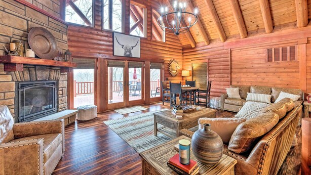 A log cabin interior with a fireplace, wooden furniture, and a chandelier. - Private Eureka Springs Cabin w/ Beaver Lake Views! (Eureka Springs)