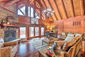 A log cabin interior with a fireplace, wooden furniture, and a chandelier. - Private Eureka Springs Cabin w/ Beaver Lake Views! (Eureka Springs)