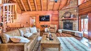 A cozy log cabin interior with a stone fireplace, leather sofa, wooden coffee table, and a chandelier. - Private Eureka Springs Cabin w/ Beaver Lake Views! (Eureka Springs)