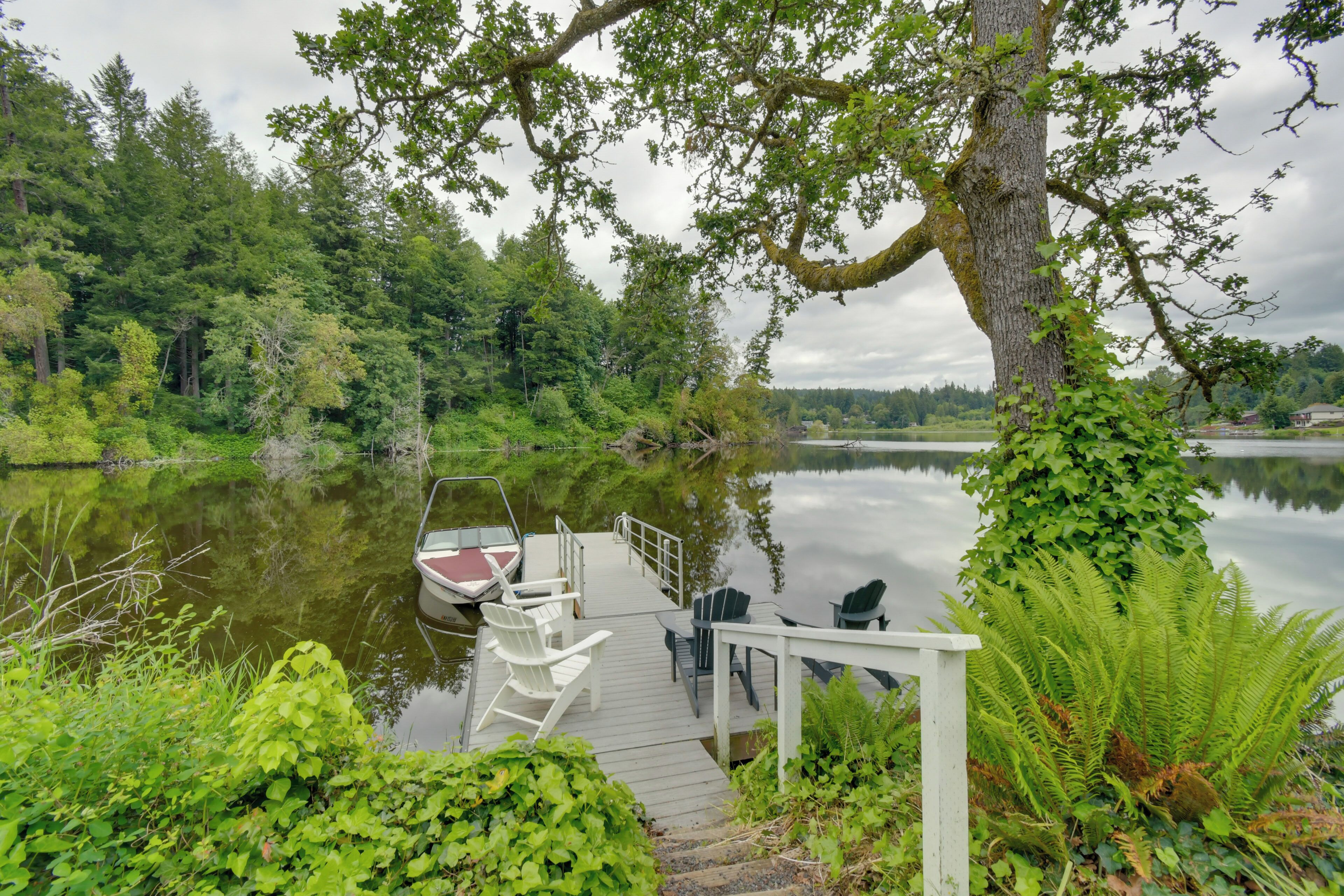 A wooden dock with chairs and a boat, surrounded by lush greenery and a calm lake.