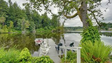 A wooden dock with chairs and a boat, surrounded by lush greenery and a calm lake.