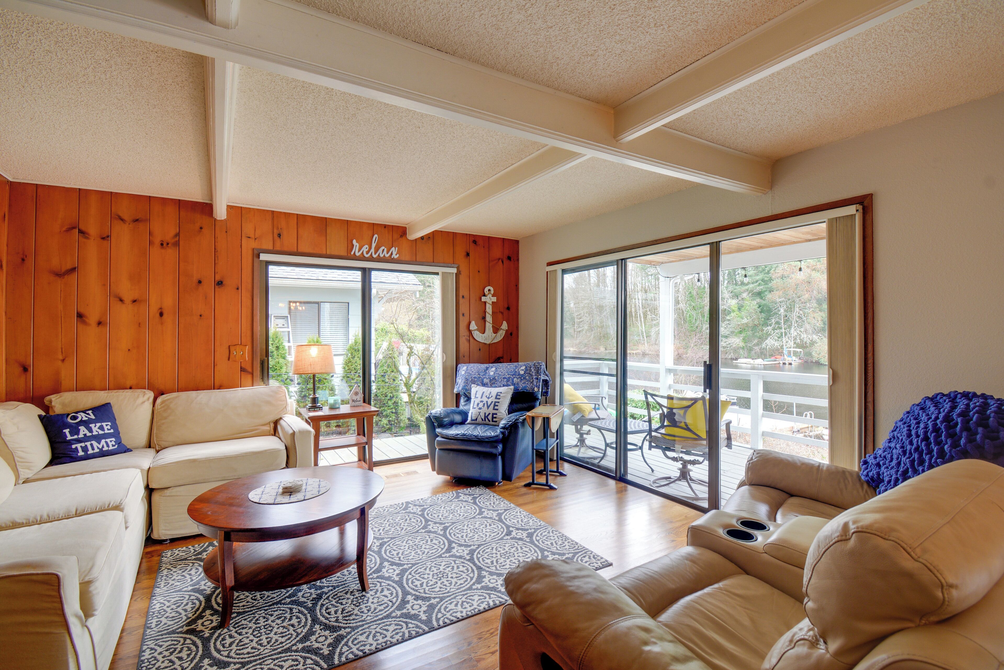 A spacious living room with a wooden wall, a sliding glass door leading to a patio, and a blue chair with a cushion.