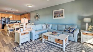 Ein Wohnzimmer mit einem hellblauen Sofa, einem weißen Couchtisch und einem Essbereich mit Holztischen und -stühlen.