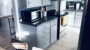 Una cocina moderna con armarios grises, horno empotrado y microondas. Hay un comedor con mesa y sillas.