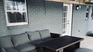 Un conjunto de sofá de mimbre con cojines, un reposapiés a juego y una mesa, todo sobre una zona de patio de hormigón.