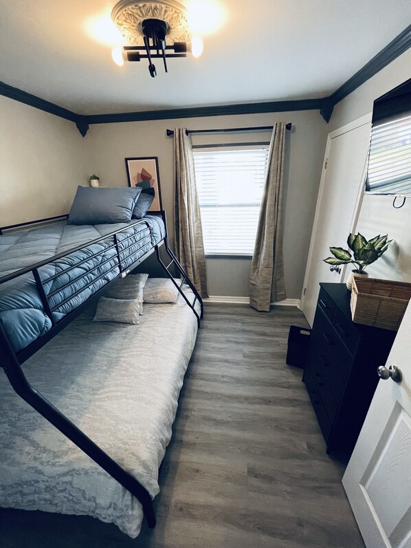 Een compacte slaapkamer met een stapelbed, een nachtkastje, een dressoir en een raam met gordijnen.