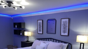 Un dormitorio con cama, mesitas de noche, decoración en la pared y una lámpara en el techo.