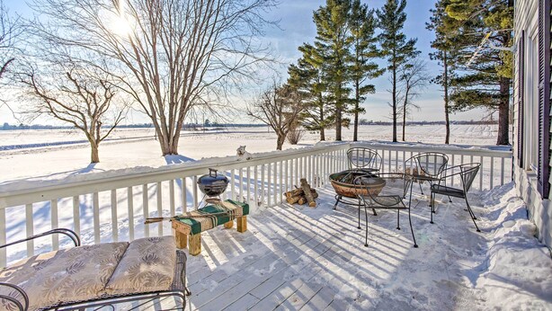Una terraza cubierta de nieve con mobiliario exterior, una parrilla y vistas a un paisaje nevado y árboles.