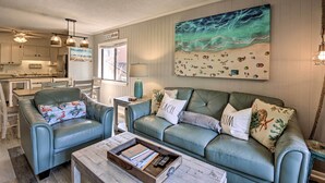 A living room with a green sofa, a coffee table, and a painting of a beach scene. - Relax by Pool & Walk to Beach: Hilton Head Condo! (Hilton Head Island)