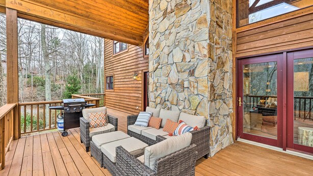 A wooden deck with wicker furniture, stone walls, and a grill. - Game Room & Fire Pit: Spacious Elk Park Lodge! (Elk Park)