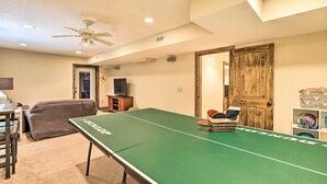 A room with a ping pong table, a ceiling fan, a television, and a door. - Game Room & Fire Pit: Spacious Elk Park Lodge! (Elk Park)