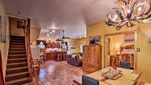 A spacious living area with a wooden staircase, a dining table with placemats, and a chandelier. - Ouachita River Cabin: Royal Haven w/ Dock! (Royal)