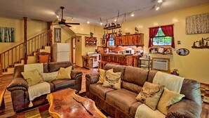 A cozy living room with a fireplace, wooden furniture, and a kitchen area in the background. - Ouachita River Cabin: Royal Haven w/ Dock! (Royal)