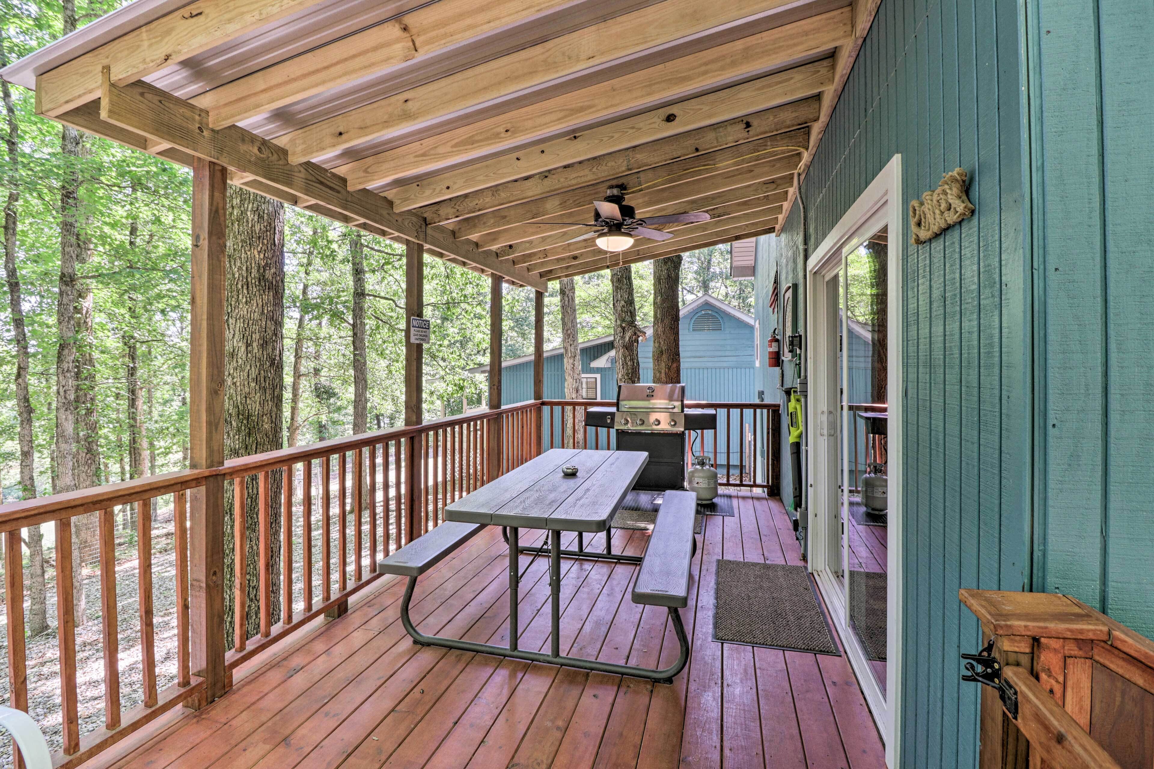 A covered deck with a picnic table and grill, surrounded by trees.