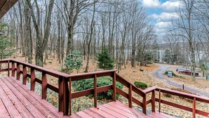 A wooden deck with a view of a forest and a road.