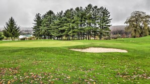 A golf course with a sand bunker, trees, and a cloudy sky.