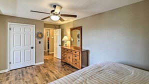 A bedroom with a wooden floor, a bed with striped bedding, a dresser with a mirror, and a ceiling fan.