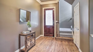 A hallway with wooden flooring, a dark wooden door, a white door, a small console table with a plant, and a mirror on the wall. - Spacious Home w/ Patio: 5 Mi to Memorial Park (Houston)