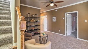 A carpeted hallway with a staircase, a ceiling fan, a chair, a small table, and a bookshelf. - Spacious Home w/ Patio: 5 Mi to Memorial Park (Houston)
