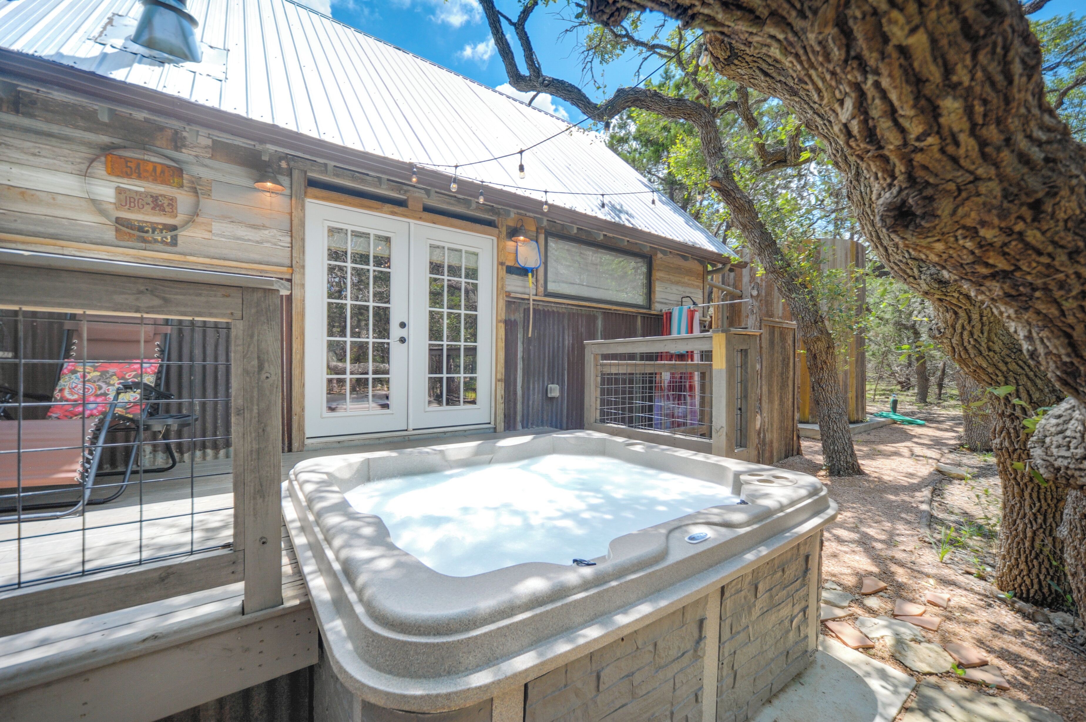 A rustic cabin with a hot tub, wooden deck, and a large tree in the background.