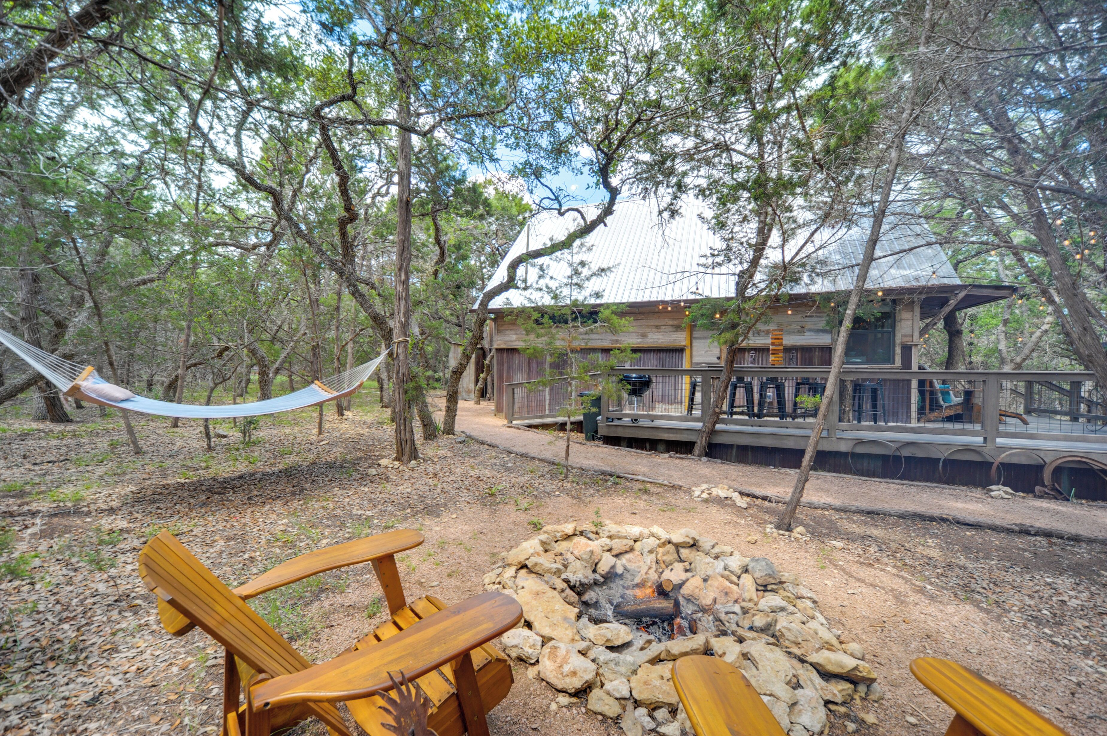 A rustic cabin with a fire pit, wooden furniture, and a hammock in a wooded area.