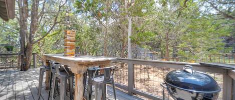 A wooden deck with a barbecue grill and a brick oven, surrounded by trees.