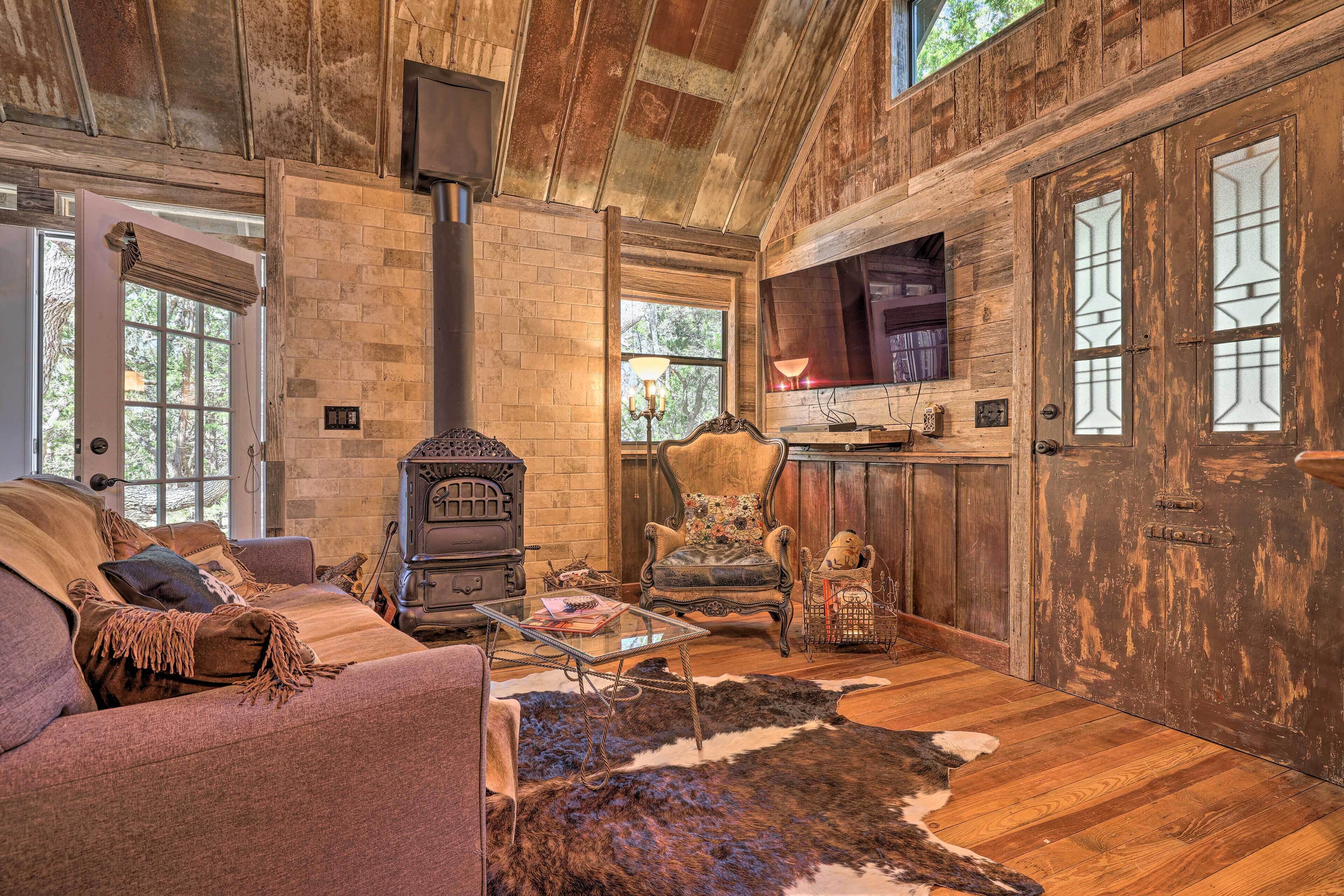 A rustic cabin interior with a stone fireplace, wooden walls, a leather sofa, and a cowhide rug.