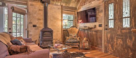 A rustic cabin interior with a stone fireplace, wooden walls, a leather sofa, and a cowhide rug.
