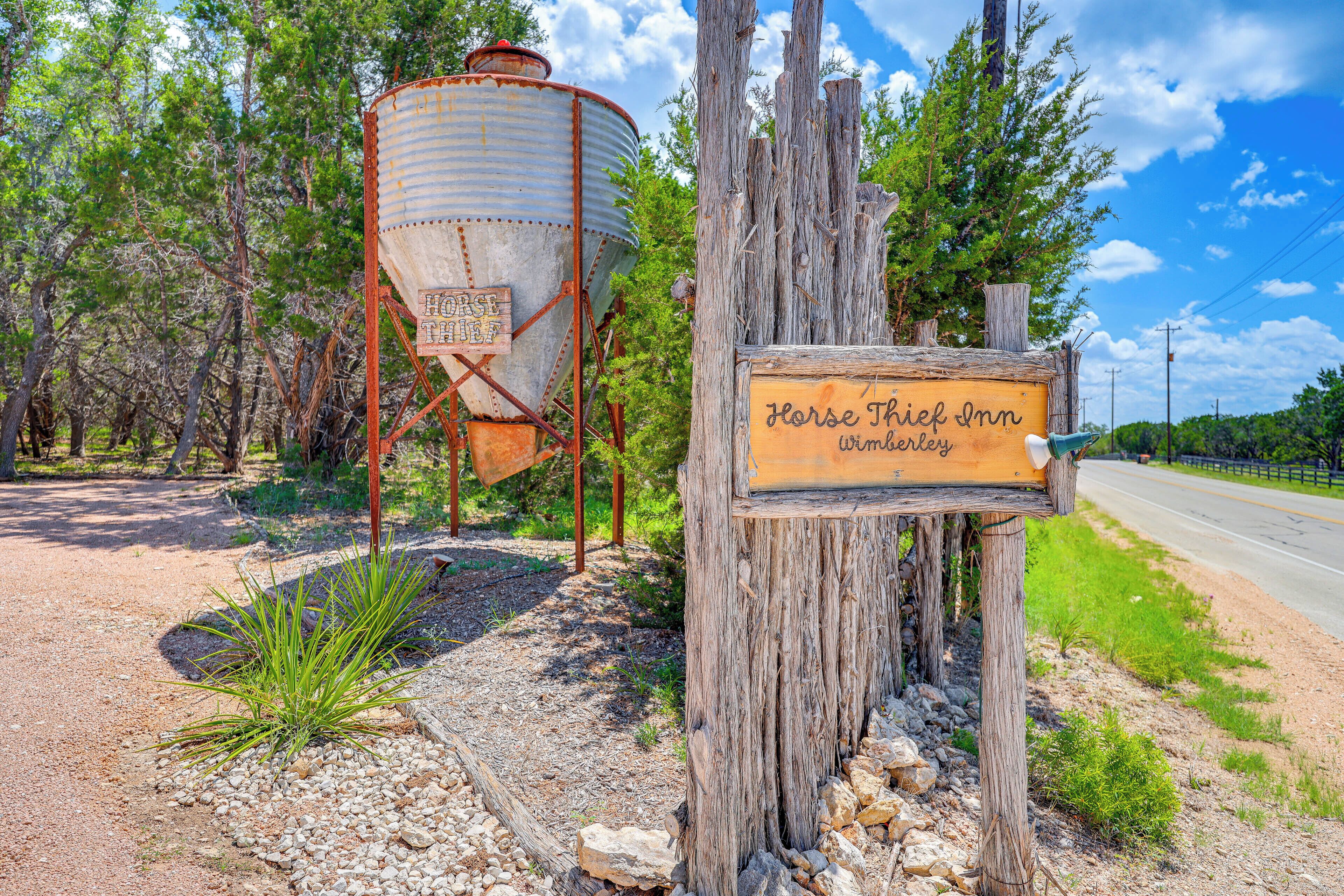 A rustic wooden sign for Horse Thief Inn in Wimberly, with a large metal water tank in the background.