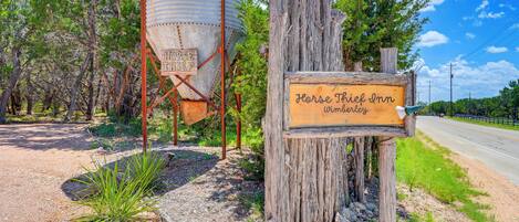 A rustic wooden sign for Horse Thief Inn in Wimberly, with a large metal water tank in the background.