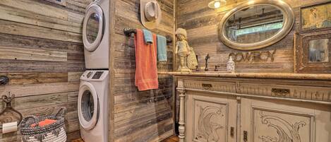 Un baño rústico con paredes de madera, lavadora, tocador con espejo y decoración temática vaquera.