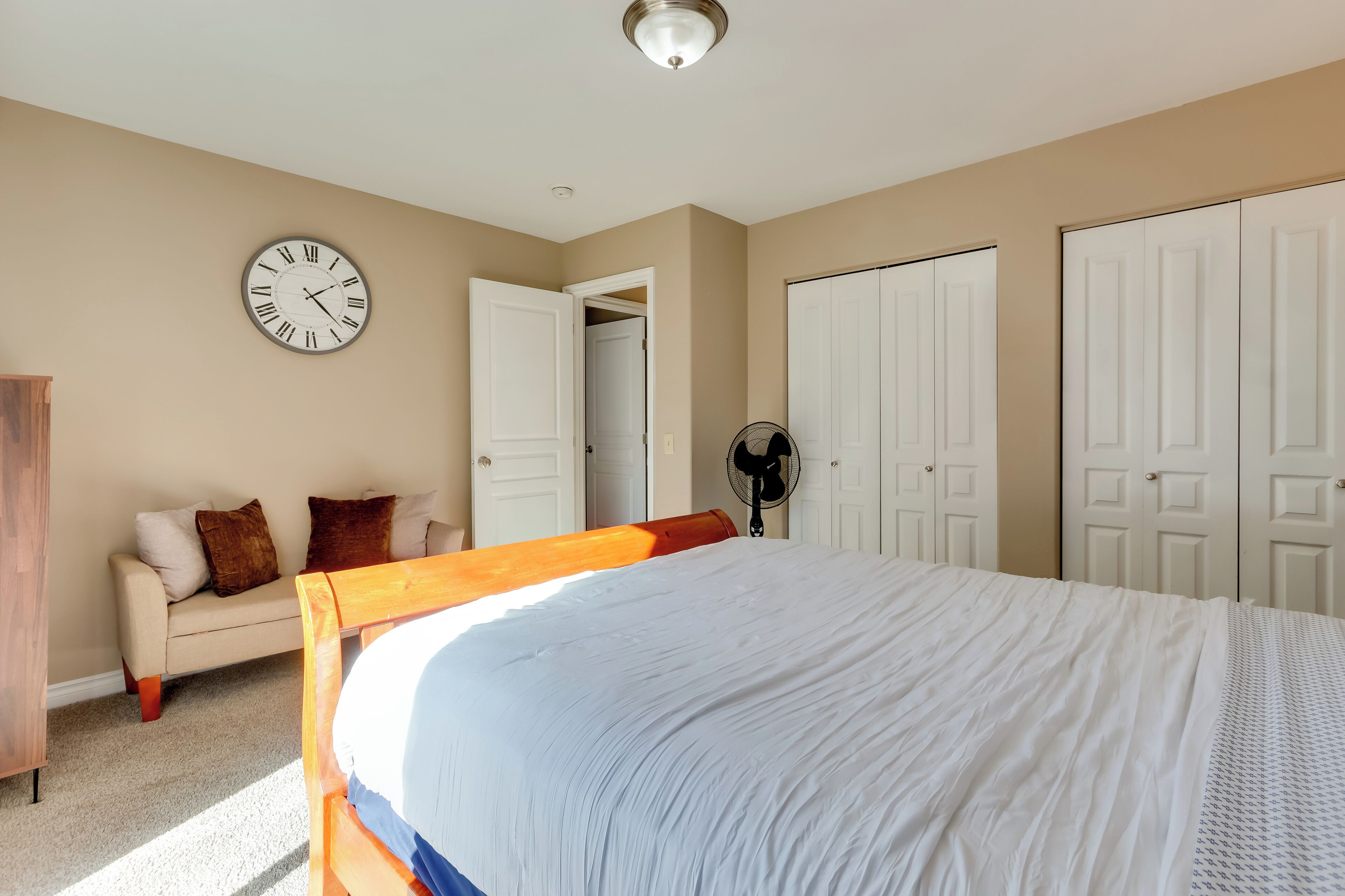 Una camera da letto con un letto, una sveglia, una ventola e un armadio.