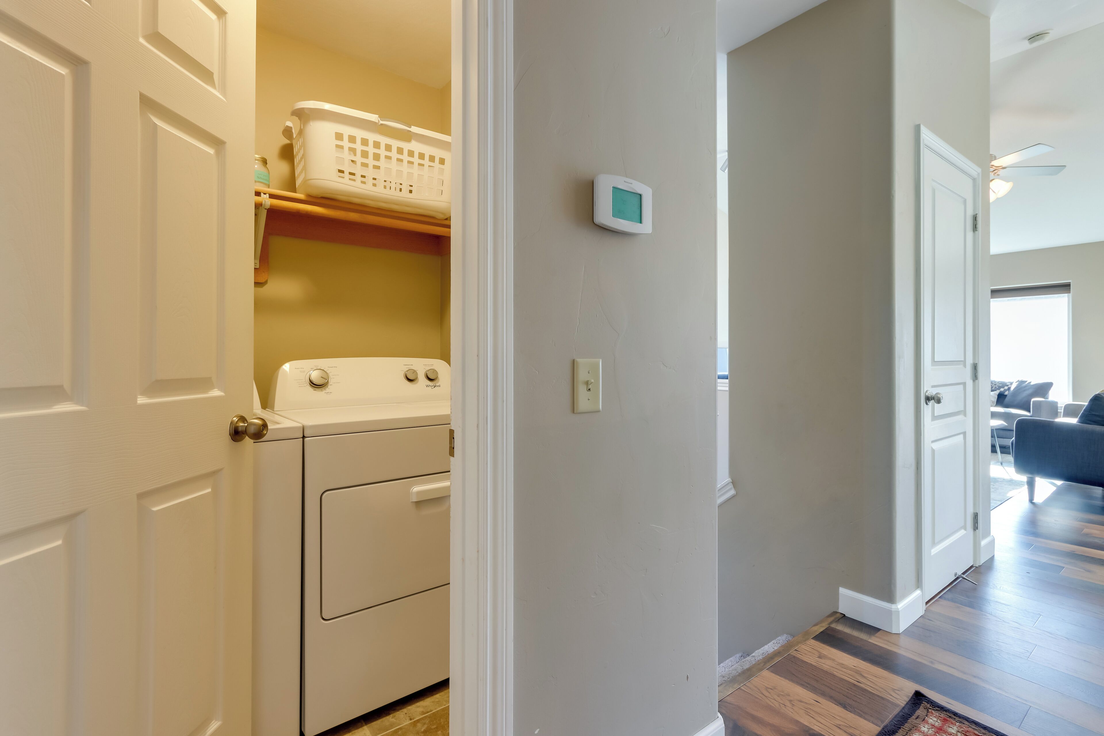 A laundry room with a washer and dryer, a thermostat, and a basket on a shelf.