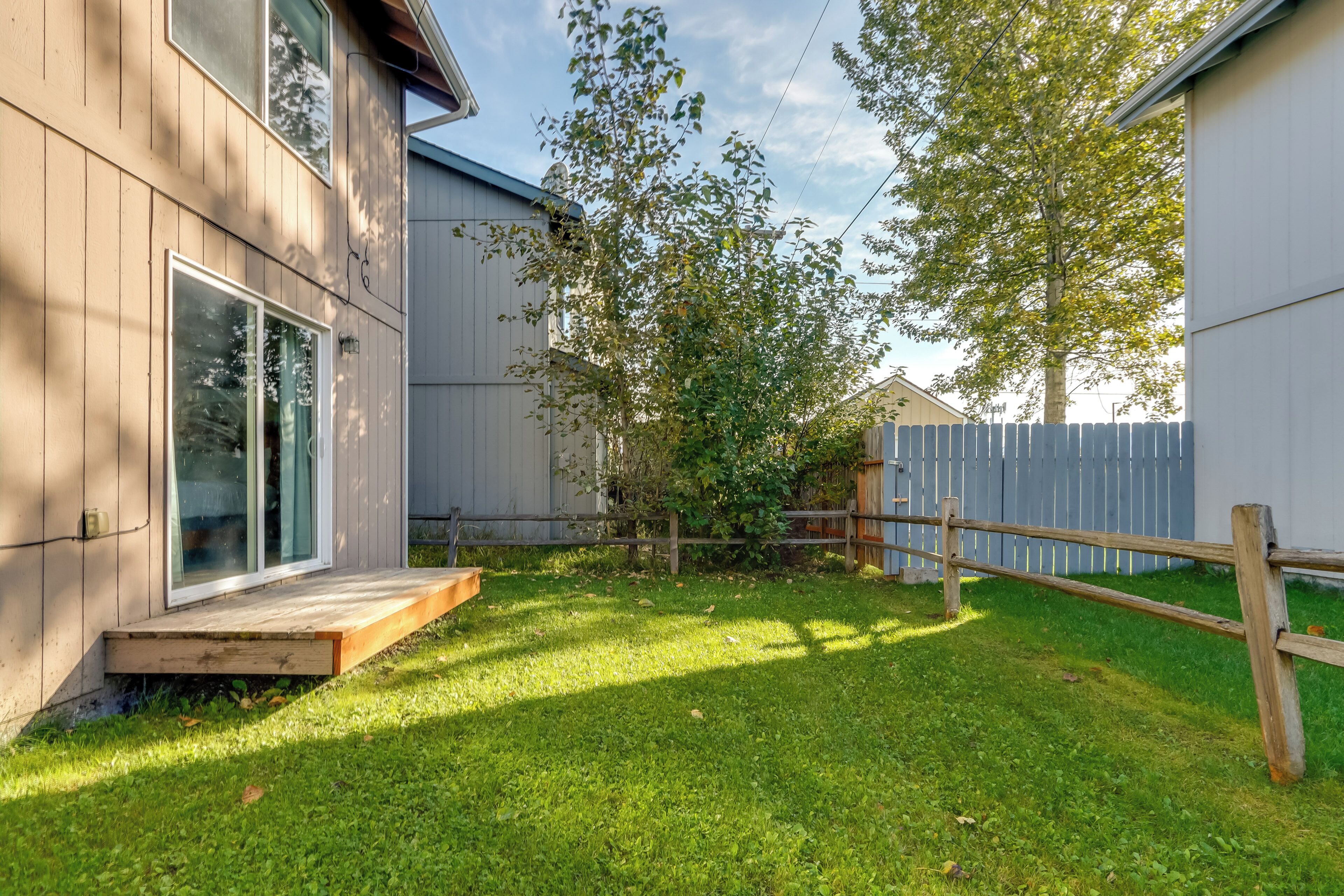 A backyard with a wooden deck, a small tree, and a wooden fence.