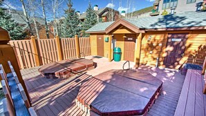 A wooden deck with a hot tub, a covered seating area, and a small building with a door and windows.