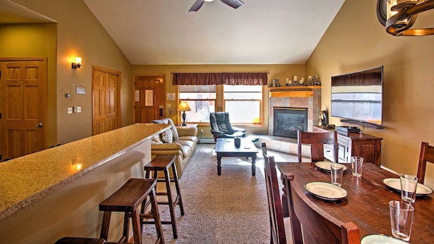 A spacious living room with a fireplace, a dining area with a wooden table set for four, and a kitchen area with a countertop and bar stools.