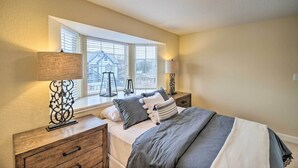 A bedroom with a large window, a bed with grey bedding, two bedside tables with lamps, and a ceiling light fixture. - Apt w/ Balconies - Steps to Kemah Boardwalk! (Kemah)