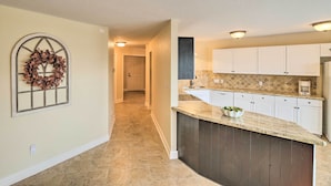 A kitchen with a marble countertop, white cabinets, and a dark backsplash. - Apt w/ Balconies - Steps to Kemah Boardwalk! (Kemah)