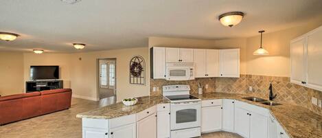 A kitchen with white cabinets, a microwave, an oven, and a sink.